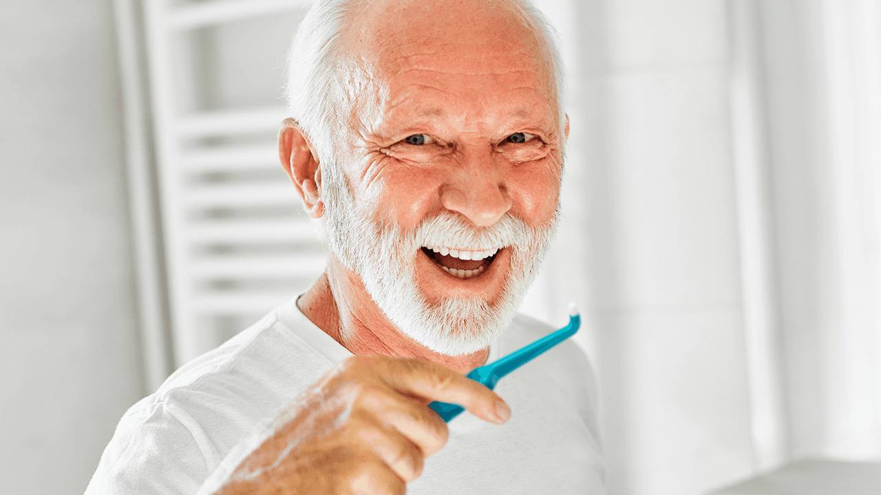 elderly man using a TePe Compact Tuft to remove plaque